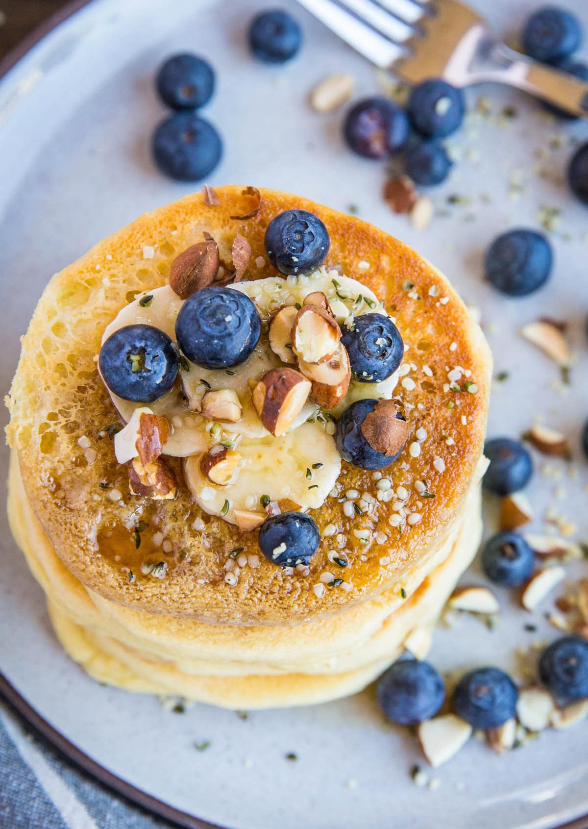 top down photo stack of almond flour pancakes on a plate with blueberries, sliced banana and honey on top.