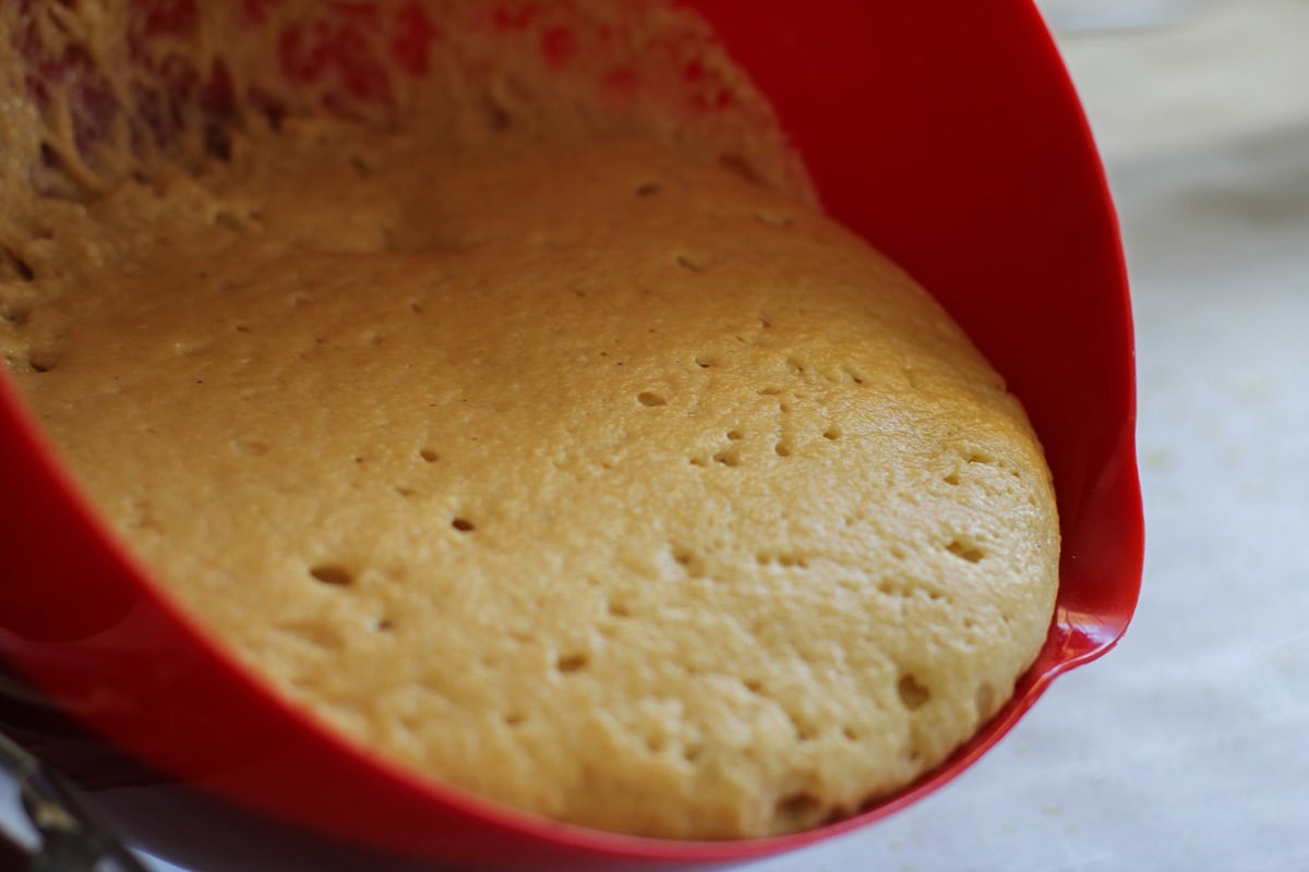 Pouring puffy almond flour pizza dough out of a large mixing bowl onto a baking sheet.