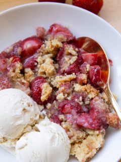 Strawberry crumble in a white bowl with vanilla ice cream, ready to eat