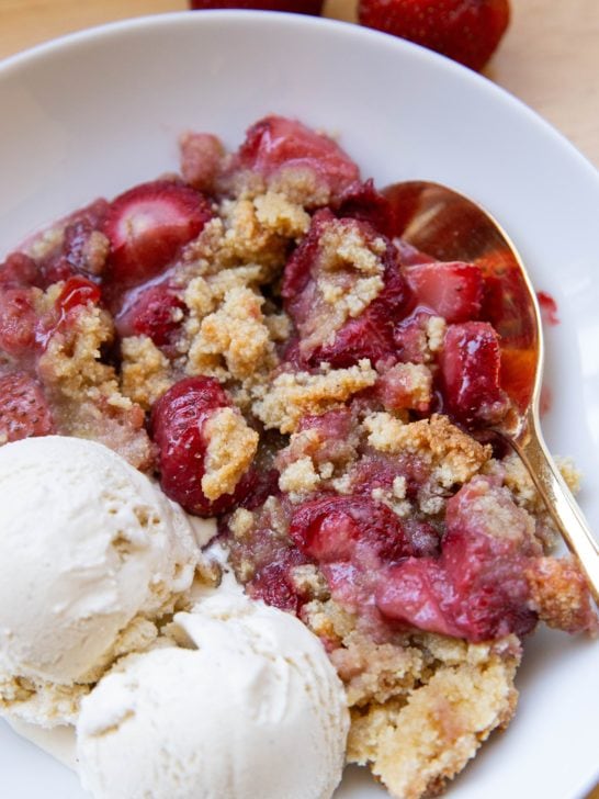 Strawberry crumble in a white bowl with vanilla ice cream, ready to eat