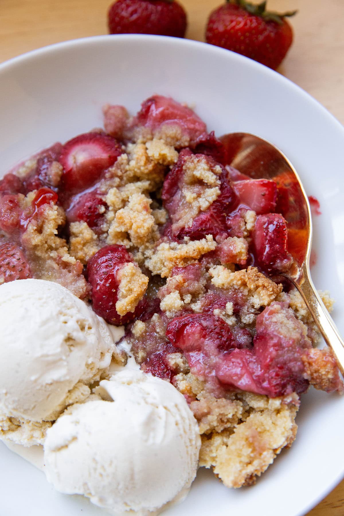 Strawberry crumble in a white bowl with vanilla ice cream, ready to eat