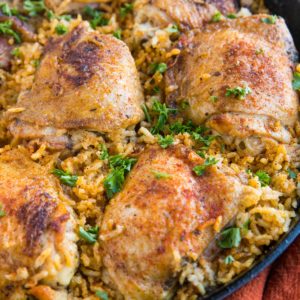 Arroz con Pollo recipe in a cast iron skillet, sprinkled with chopped fresh parsley and a red napkin to the side.