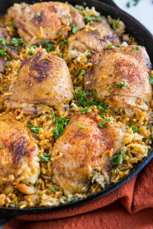 Arroz con Pollo recipe in a cast iron skillet, sprinkled with chopped fresh parsley and a red napkin to the side.