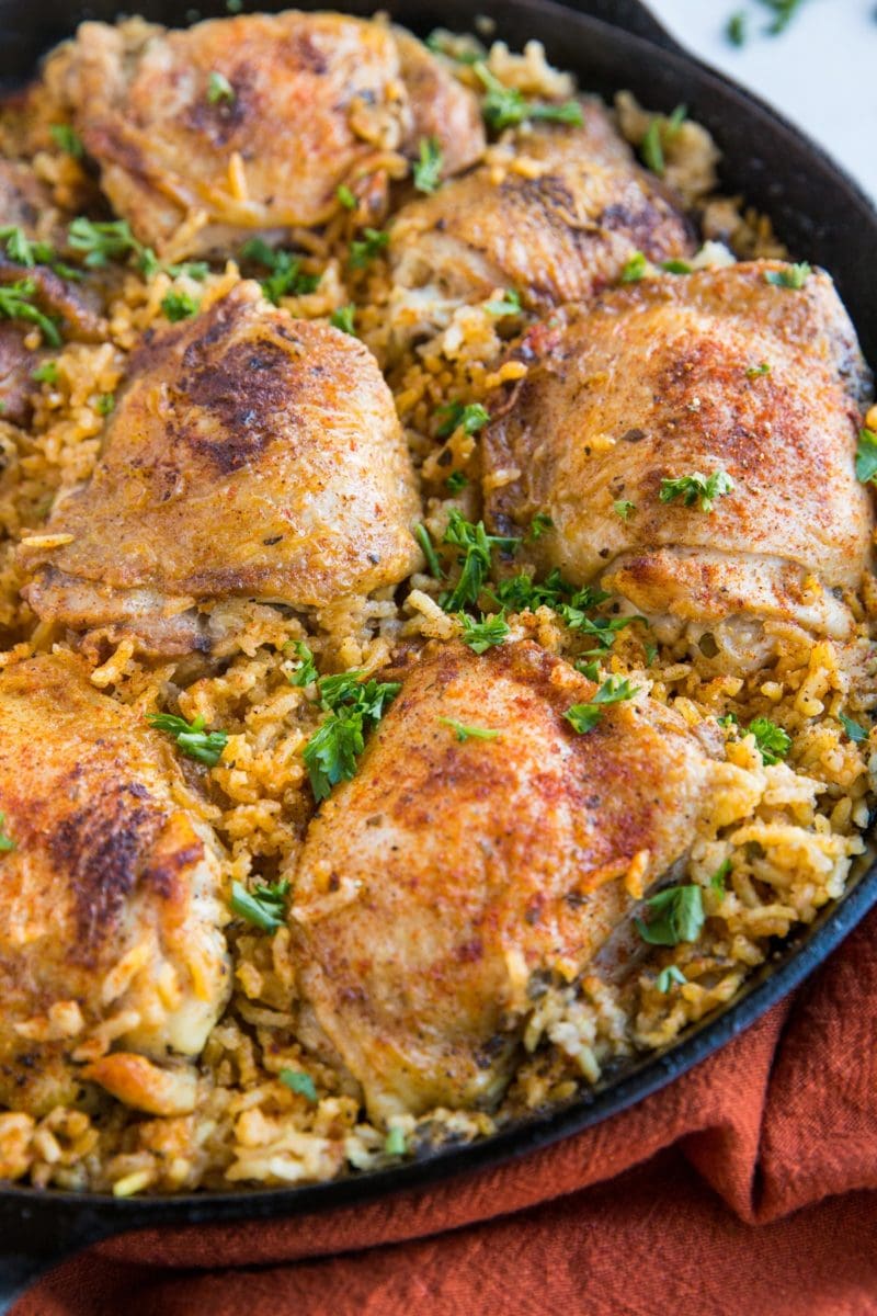 Arroz con Pollo recipe in a cast iron skillet, sprinkled with chopped fresh parsley and a red napkin to the side.