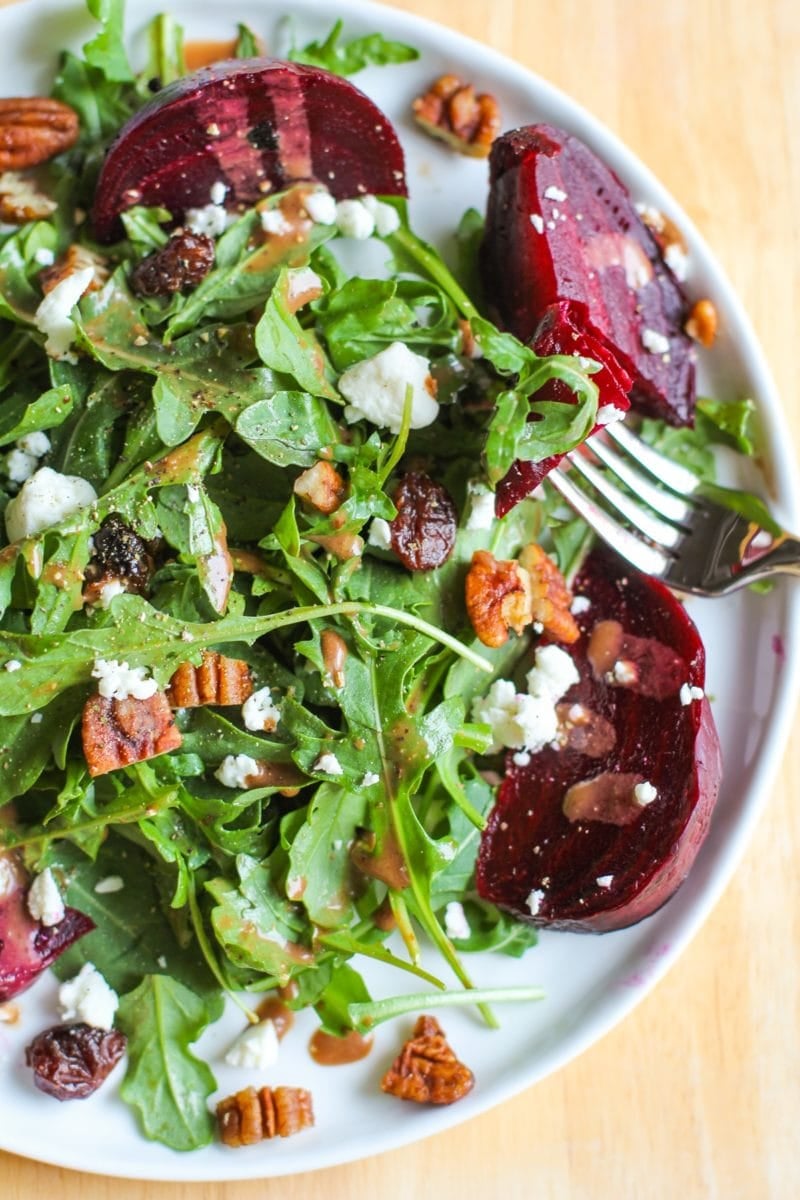 Arugula Beet Salad with pecans, cranberries, goat cheese and balsamic dressing on a white plate with a fork taking a bite.