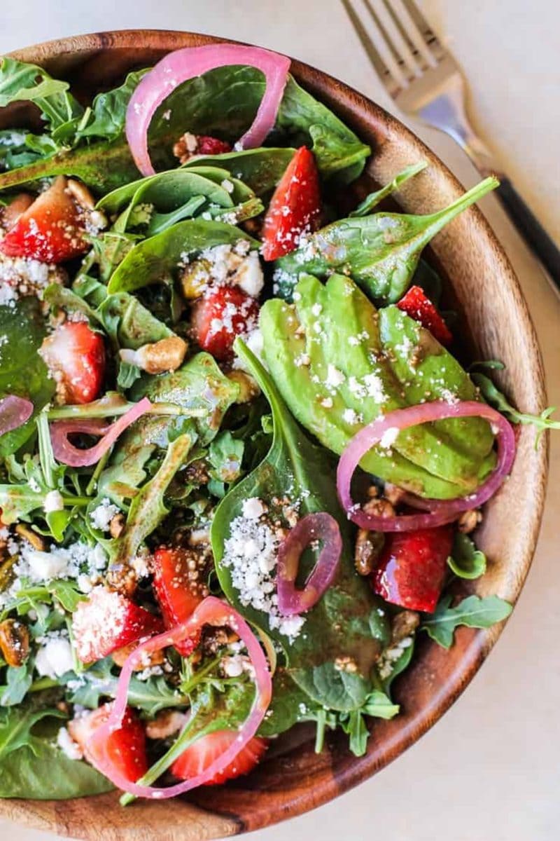Bug wooden bowl of arugula salad with pickled red onions, feta cheese, avocado, strawberries and strawberry vinaigrette