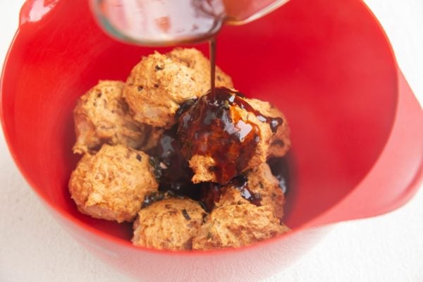 Pouring sauce over the meatballs in a mixing bowl.