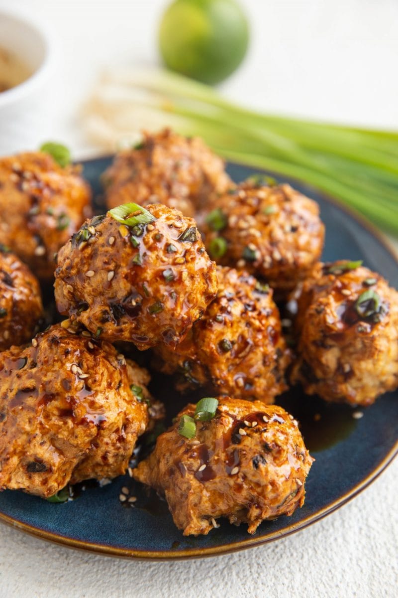 Blue plate of turkey meatballs sprinkled with sesame seeds with green onions in the background.