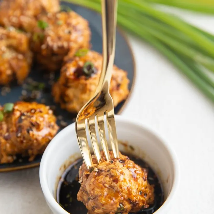 Gold fork dipping a turkey meatball into a bowl of dipping sauce.