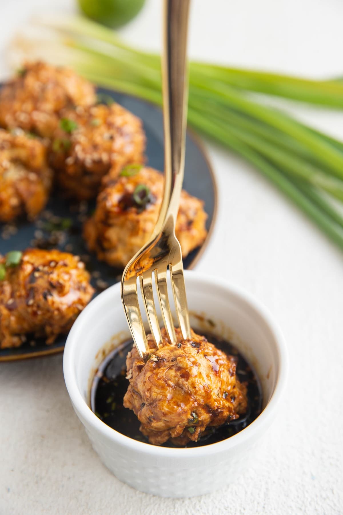 Gold fork dipping a turkey meatball into a bowl of dipping sauce.