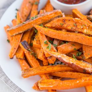 Plate of sweet potato fries with a small bowl of ketchup, sprinkled with chopped fresh parsley. Ready to serve.