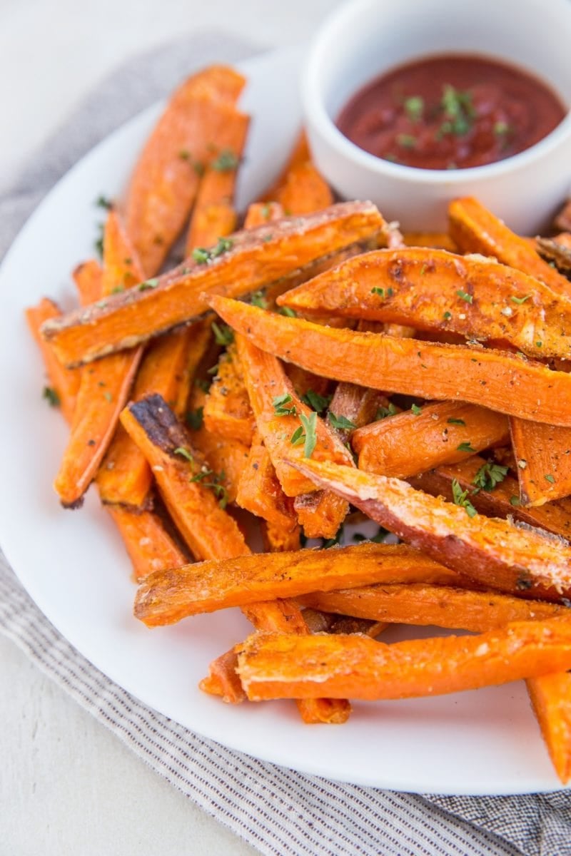 Plate of sweet potato fries with a small bowl of ketchup, sprinkled with chopped fresh parsley. Ready to serve.