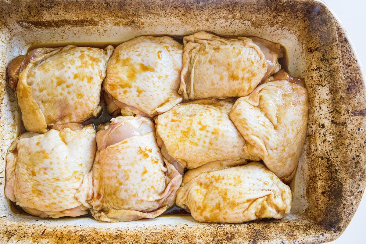 Skin on chicken thighs in a large casserole dish with teriyaki sauce.