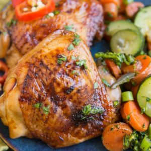 Easy Baked Teriyaki Chicken Thighs on a blue plate with a green napkin with sauteed vegetables. Ready to serve.