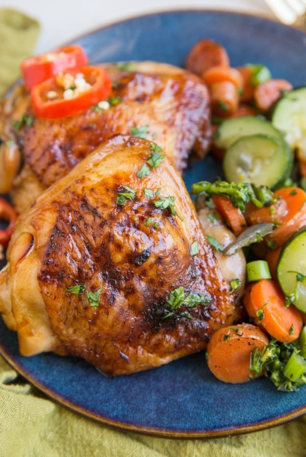 Easy Baked Teriyaki Chicken Thighs on a blue plate with a green napkin with sauteed vegetables. Ready to serve.