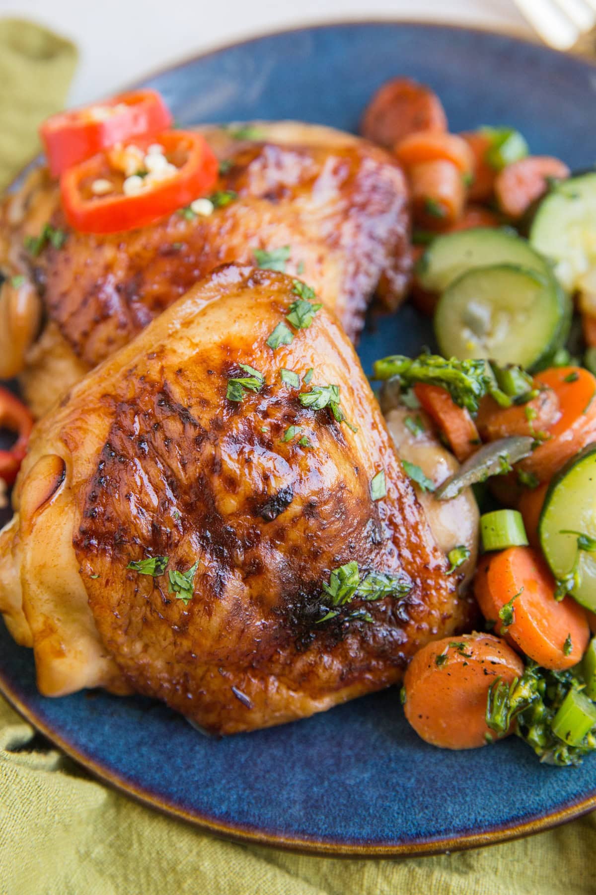 Easy Baked Teriyaki Chicken Thighs on a blue plate with a green napkin with sauteed vegetables. Ready to serve.