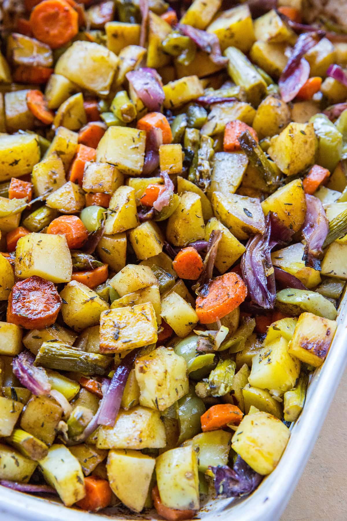A close-up of a tray filled with balsamic roasted vegetables, including potatoes, carrots, red onions, green beans, and herbs, all cut into small pieces and perfectly seasoned.