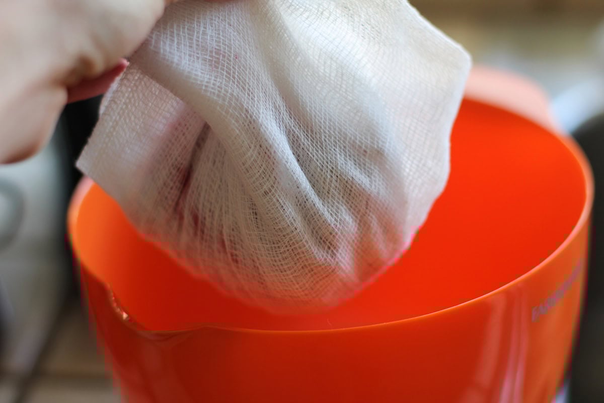 hand holding shredded beets wrapped in cheese cloth over a large bowl to squeeze the liquid out of the beets to make hash browns.