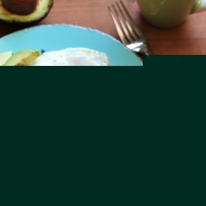 Beet Hash Browns on a blue plate with an egg and avocado on top. The plate sits on a wooden table with a cup of coffee and a fork to the side.