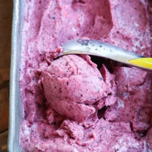 Loaf pan with berry nice cream inside and a ice cream scooper making a scoop to serve.