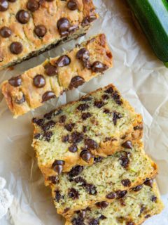 Loaf of zucchini bread on a sheet of parchment paper cut into slices.