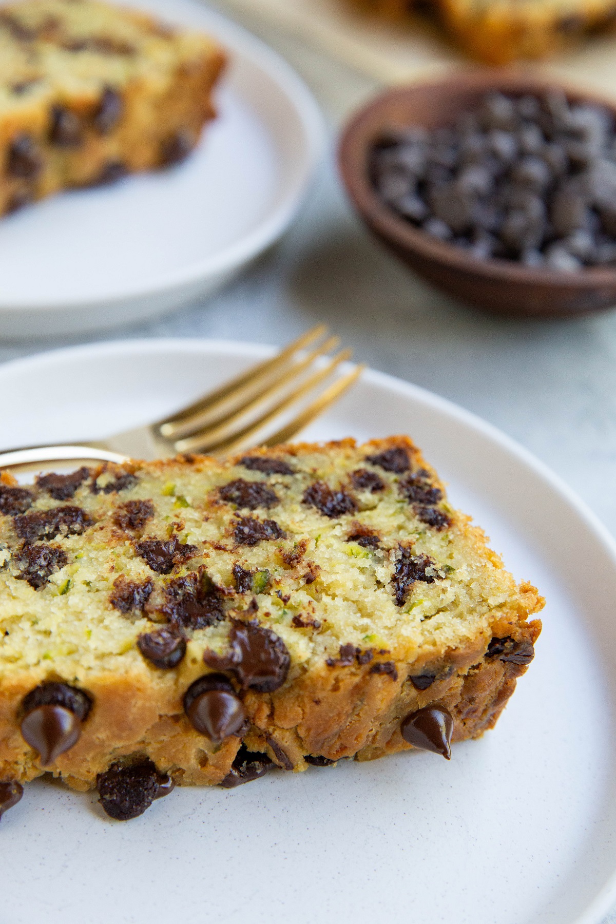 Close up image of a slice of chocolate chip zucchini bread on a white plate, ready to eat.