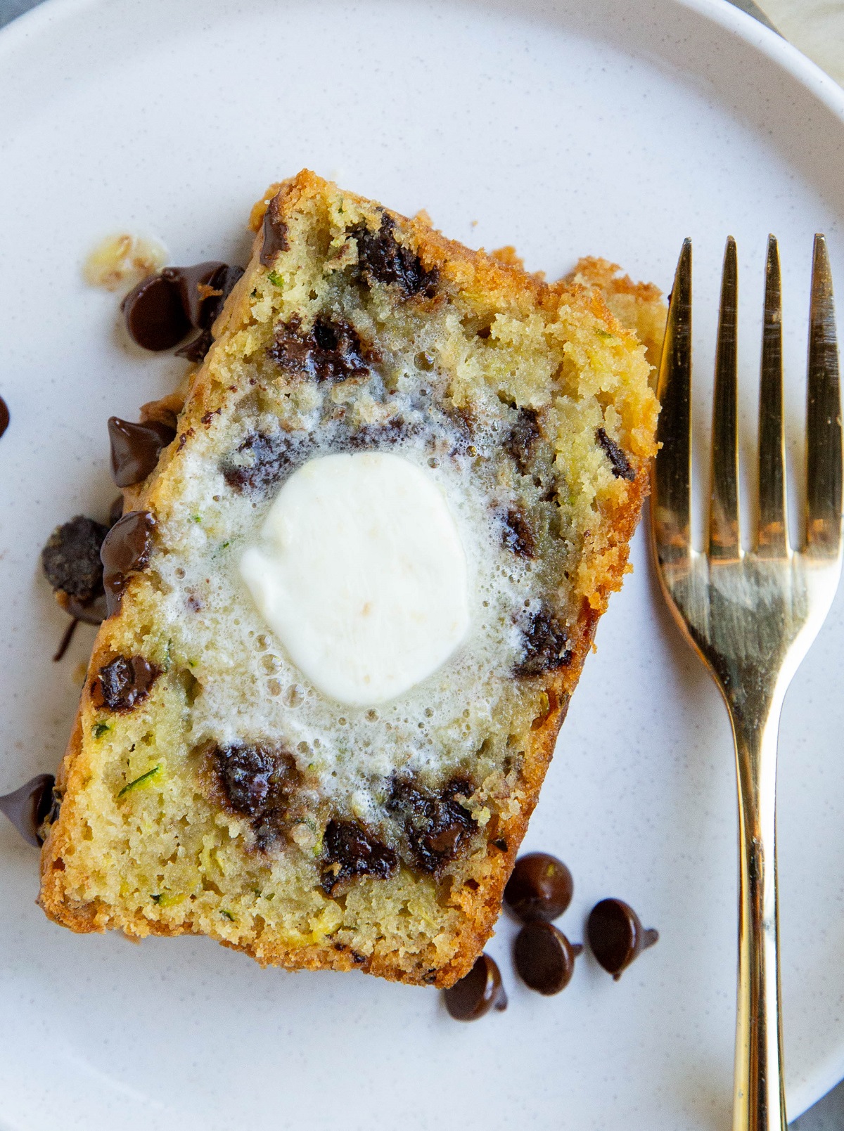 Close up on a slice of zucchini bread with melted butter on top, ready to eat.