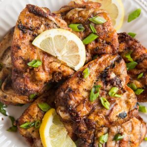 White plate stacked with grilled chicken sprinkled with chopped green onions, ready to serve.