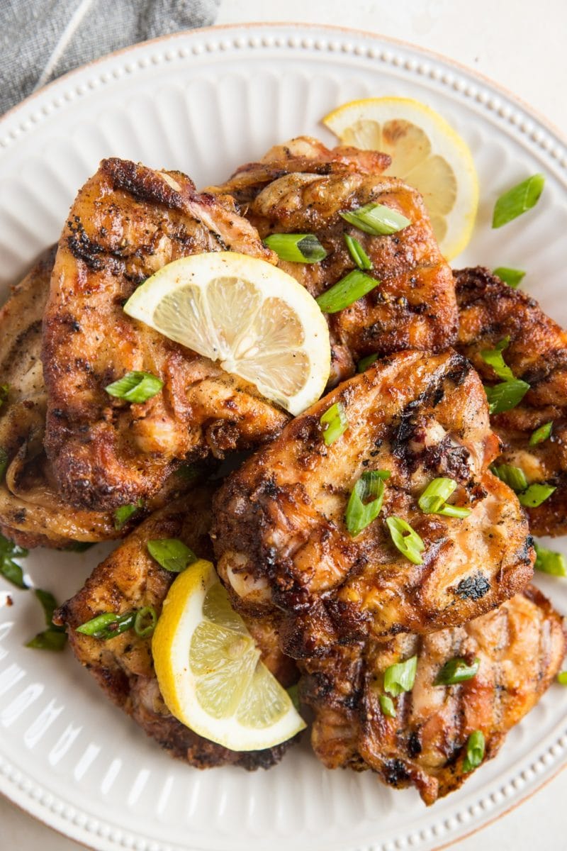 White plate stacked with grilled chicken sprinkled with chopped green onions, ready to serve.