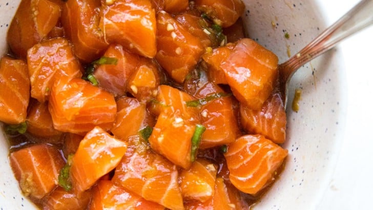 Bowl of salmon poke with a spoon in it on a white surface