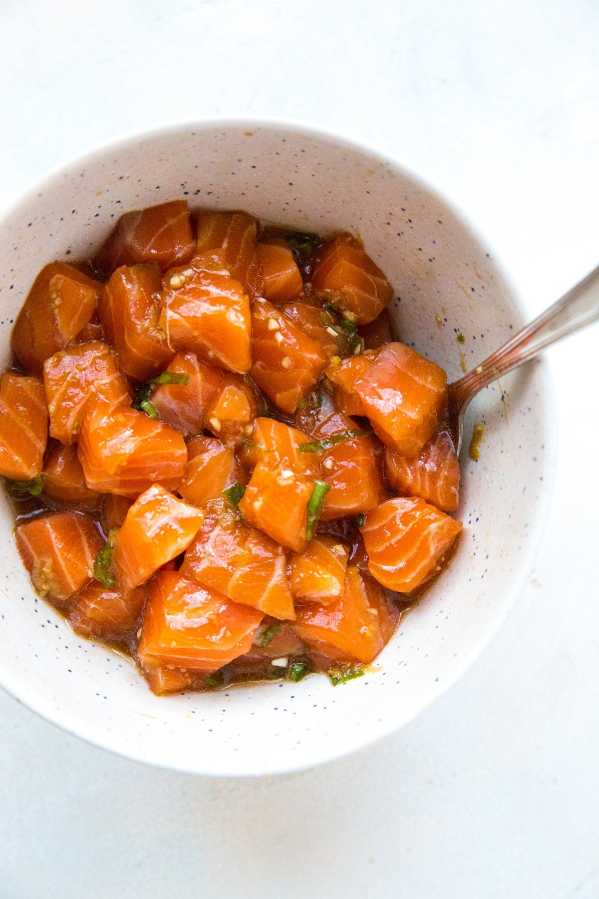 Bowl of salmon poke with a spoon in it on a white surface