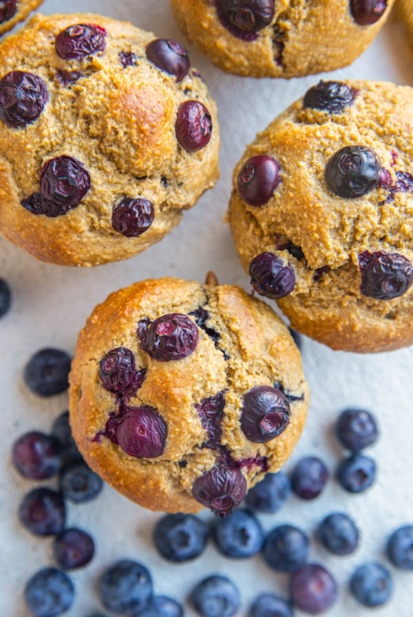 Close up of oatmeal banana blueberry muffins sitting on a white background with fresh berries all around.