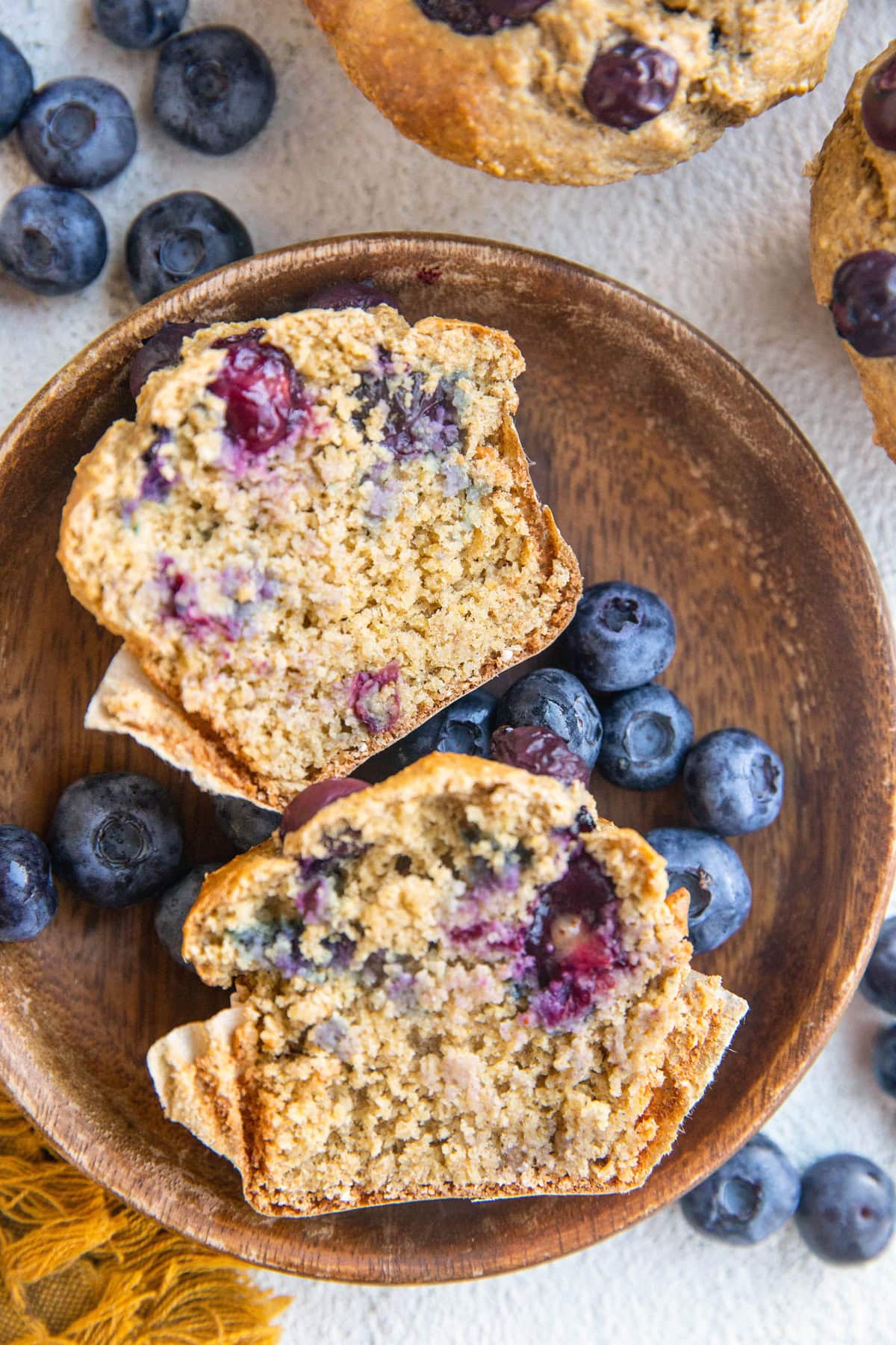 Plate with a muffin sliced in half and a hand picking up one of the halves, with full muffins in the background.