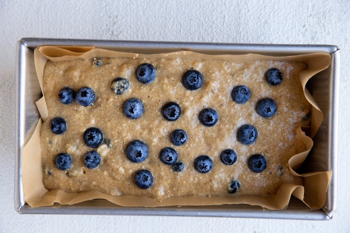 blueberry oatmeal bread batter in a loaf pan with blueberries on top, ready to go into the oven.