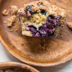 Two wooden plates with blueberry muffins on each, one muffin sliced in half so you can see the fluffy inside with fresh blueberries.