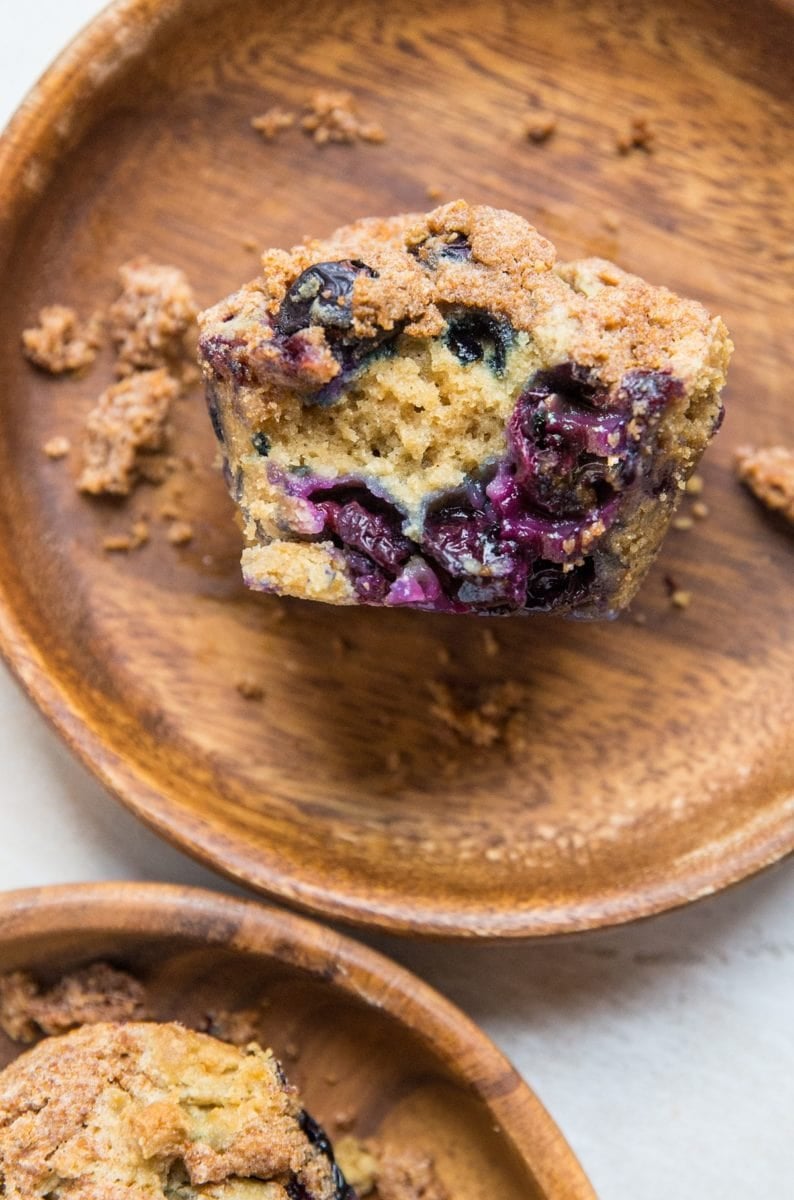 Two wooden plates with blueberry muffins on each, one muffin sliced in half so you can see the fluffy inside with fresh blueberries.