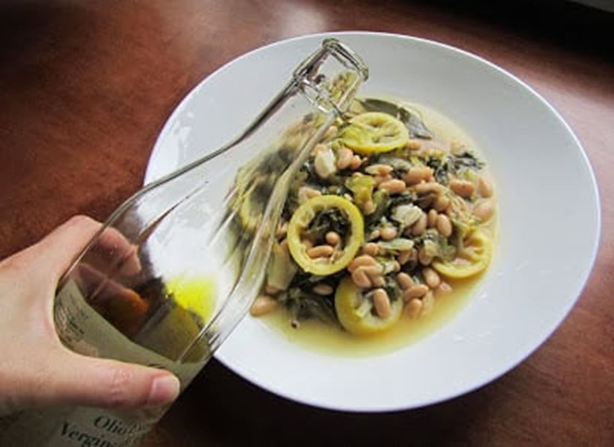 Hand pouring a little olive oil over braised escarole