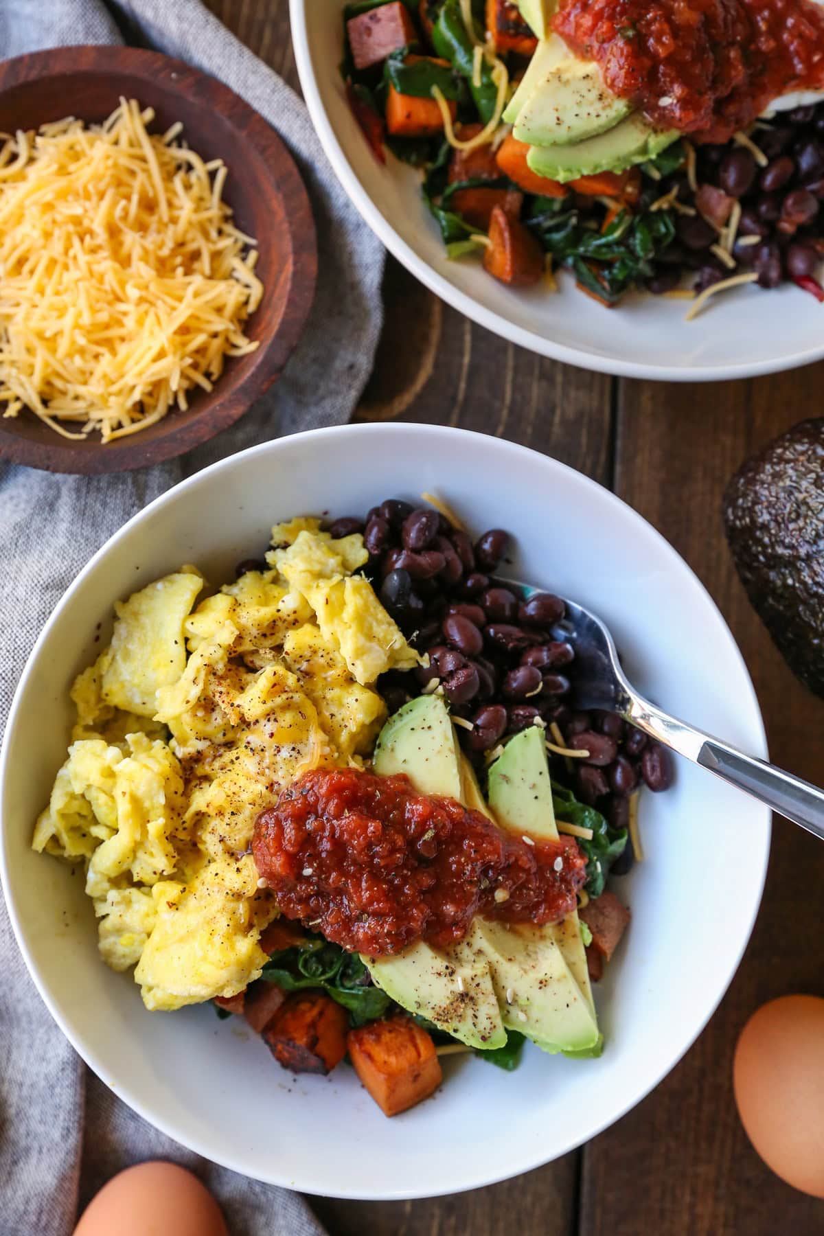 Breakfast bowl with sweet potatoes, kale, eggs, black beans, avocado, and salsa. Ready to eat.