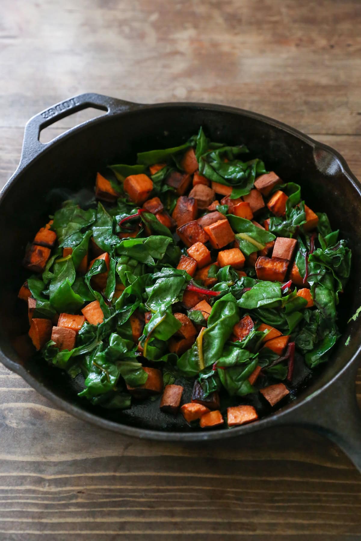Cast iron skillet full of cubed sweet potatoes and kale to make breakfast bowls.