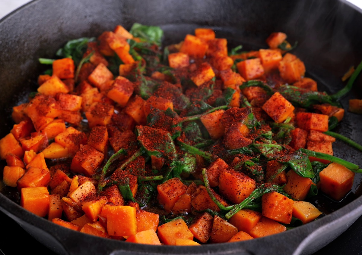 Cast iron skillet with sweet potatoes, spinach, and chili powder cooking to make breakfast tacos