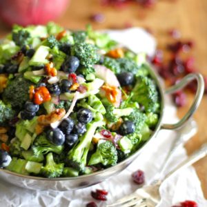 Broccoli salad in a bowl with dried cranberries to the side and forks to the side.