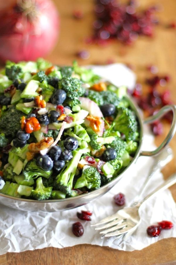 Broccoli salad in a bowl with dried cranberries to the side and forks to the side.