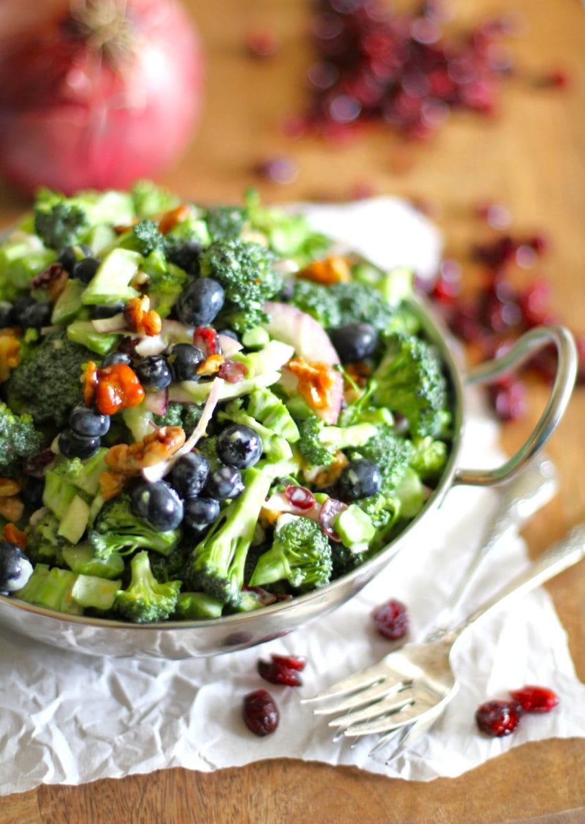 Broccoli salad in a bowl with dried cranberries to the side and forks to the side.