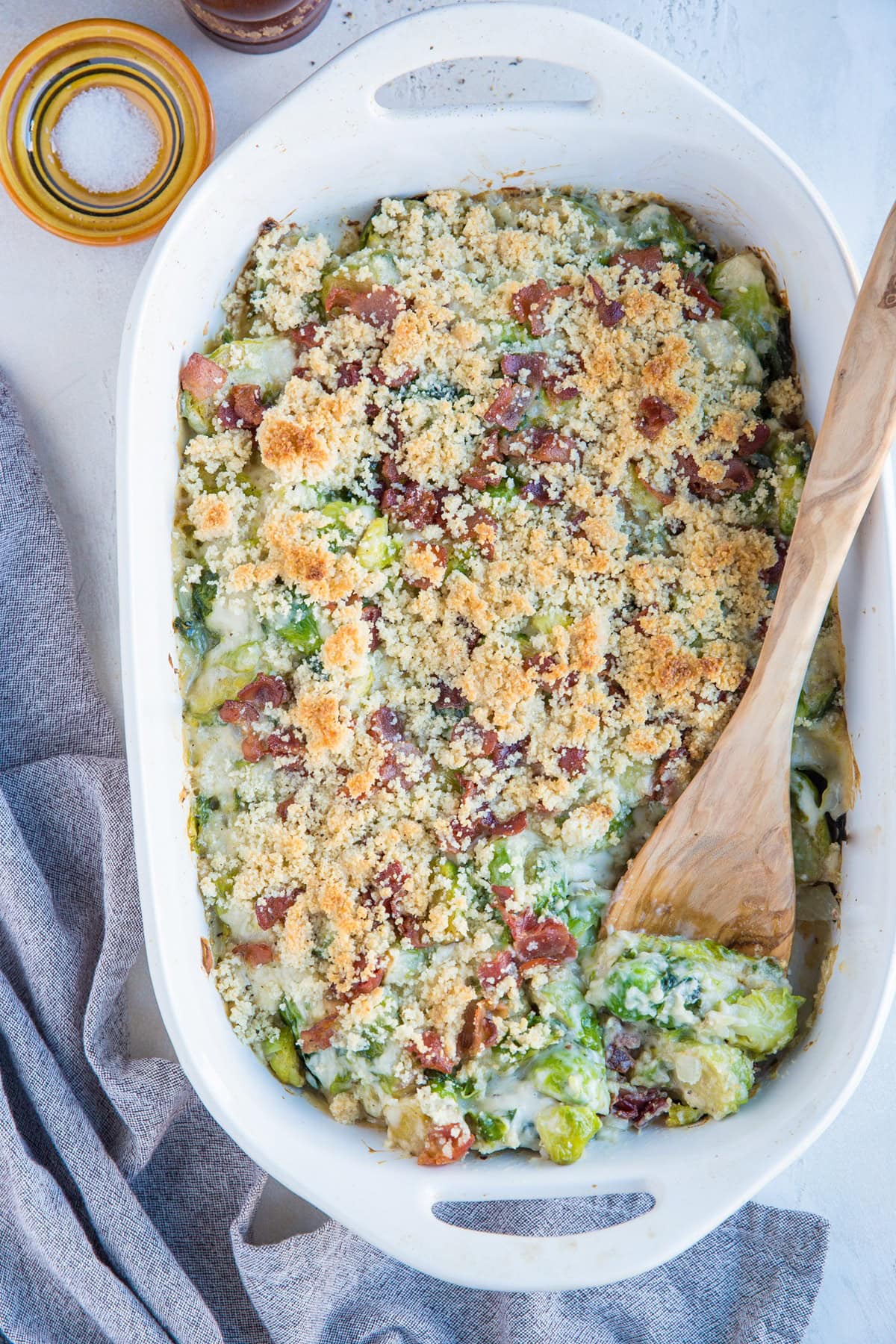 Brussel sprout casserole in a large white casserole dish with a grey napkin to the side.
