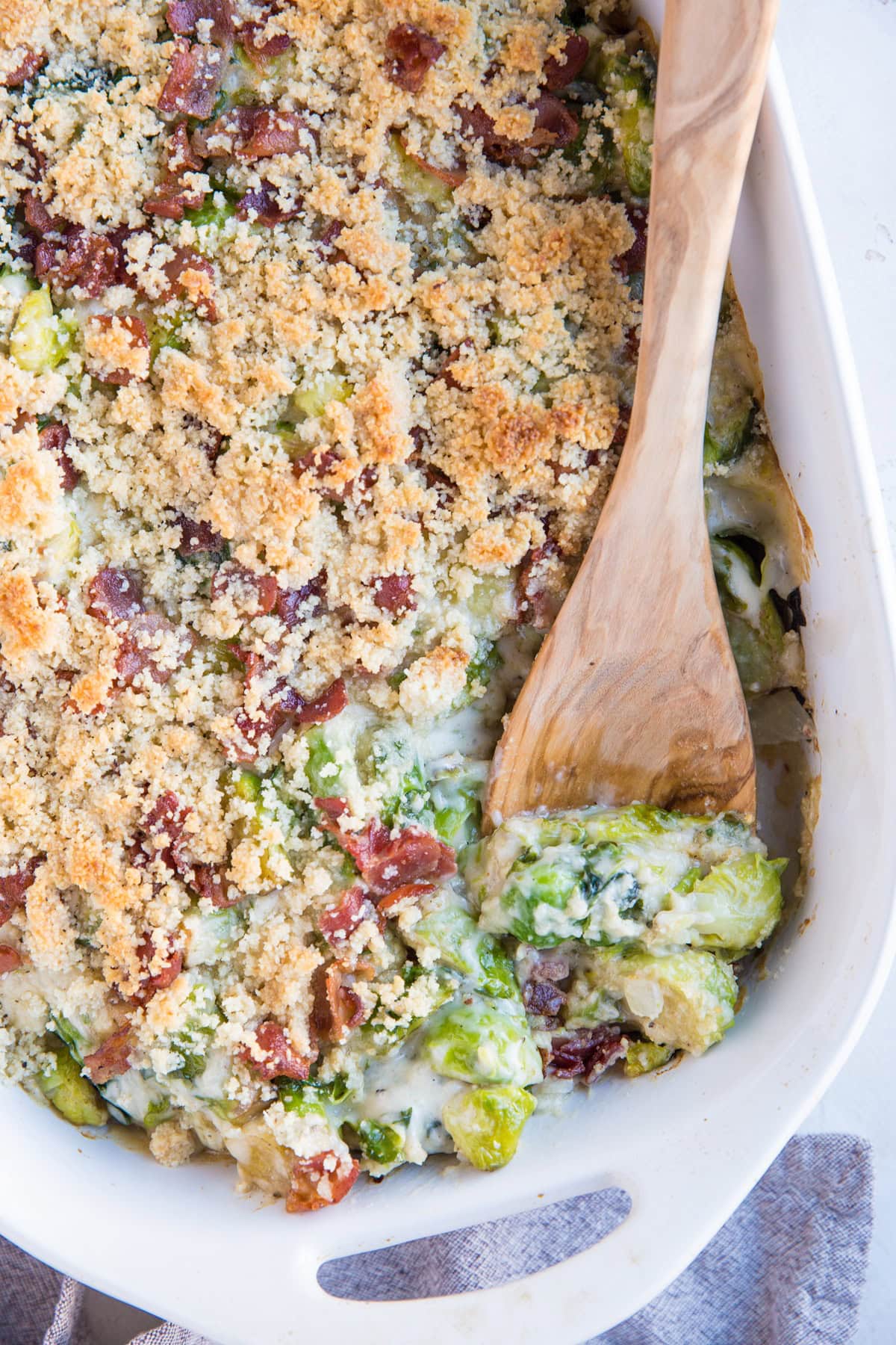Creamy Brussel Sprout Casserole in a large white casserole dish with a grey napkin to the side.