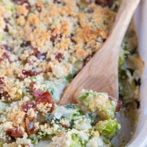Large casserole dish full of creamy brussel sprout casserole with a wooden spoon scooping out some of the casserole.