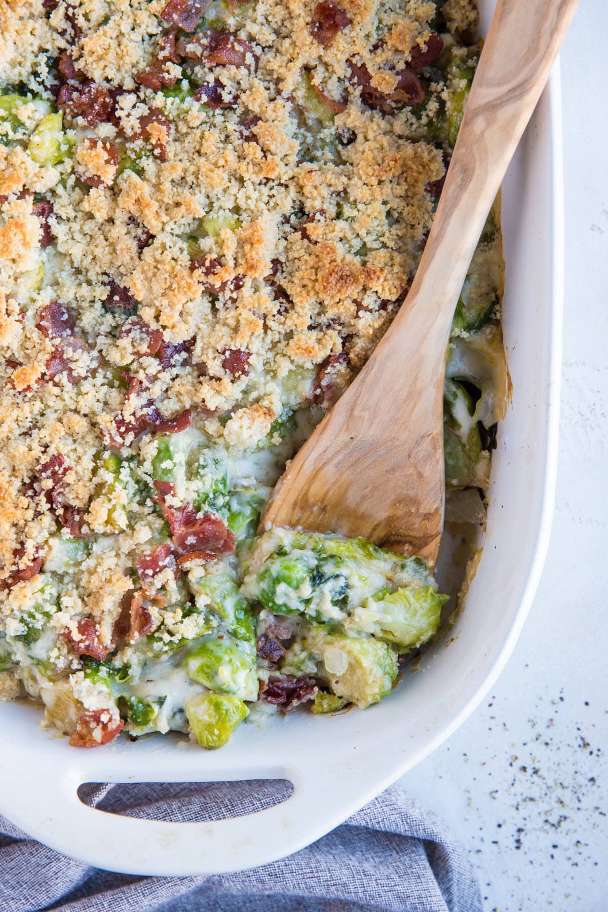 Grain-Free Keto Brussel Sprout Casserole with Bacon in a big white casserole dish with a grey napkin to the side, ready to serve.