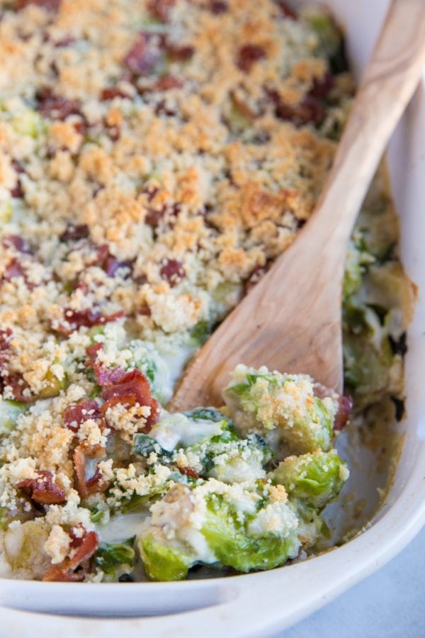 Large casserole dish full of creamy brussel sprout casserole with a wooden spoon scooping out some of the casserole.