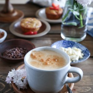 Mug of bulletproof coffee with cacao nibs to the side and muffins in the background.