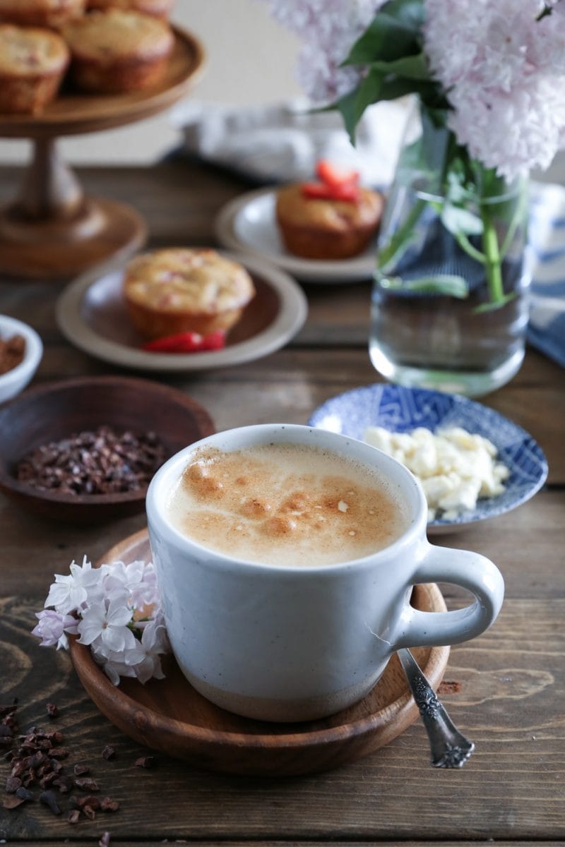 Mug of bulletproof coffee with cacao nibs to the side and muffins in the background.